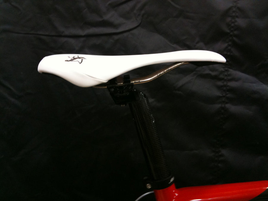 Close-up of a white road saddle and seatpost on a red frame against a black background