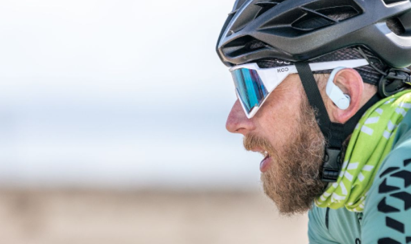 Side profile of a bearded cyclist in a helmet, sunglasses and green jersey