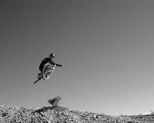 Black-and-white shot of a rider whipping a mountain bike in mid-air over a rocky ridge