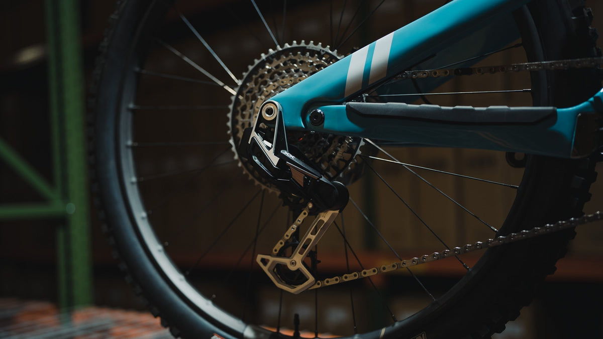 Close-up of a rear derailleur, cassette and chain on a teal mountain bike frame