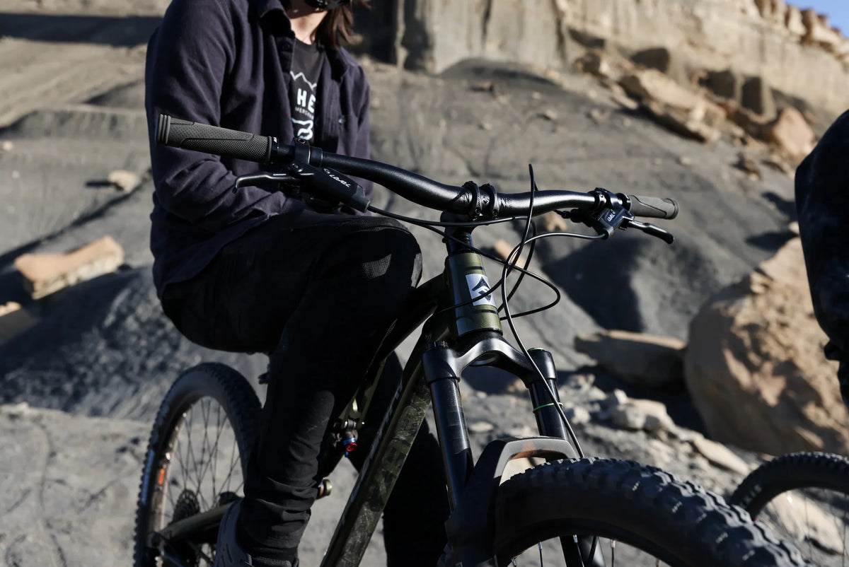 Rider in a dark hoodie on a mountain bike seen from the chest down, handlebar and fork over rocky terrain