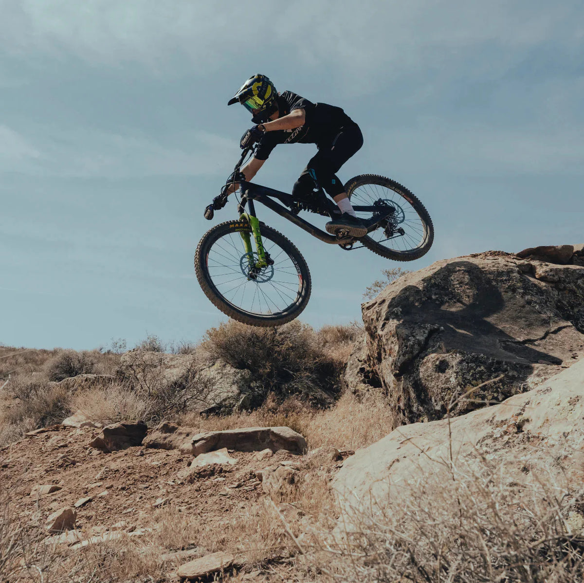 Rider in a full-face helmet jumping a mountain bike over desert rocks against a blue sky