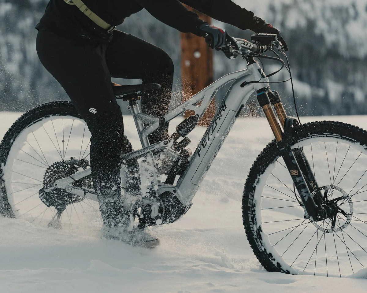 Close-up of a rider on a silver electric mountain bike kicking up snow