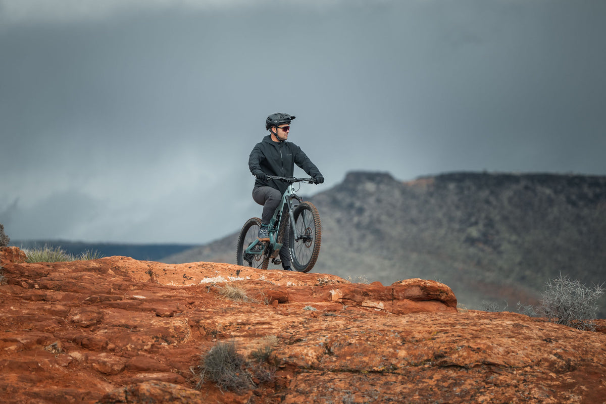 Rider on a mountain bike on red rock under stormy skies with a mesa in the distance