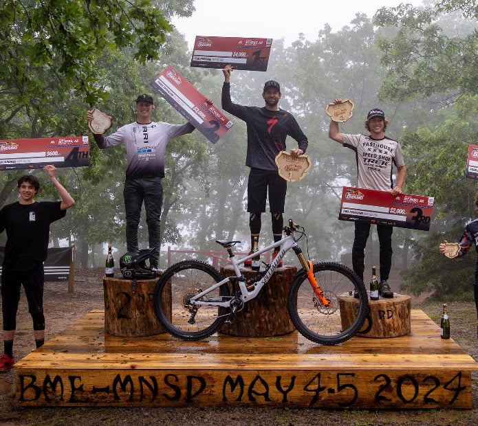 Podium of three racers holding prize checks and plaques with an Ari mountain bike, BME May 4-5 2024