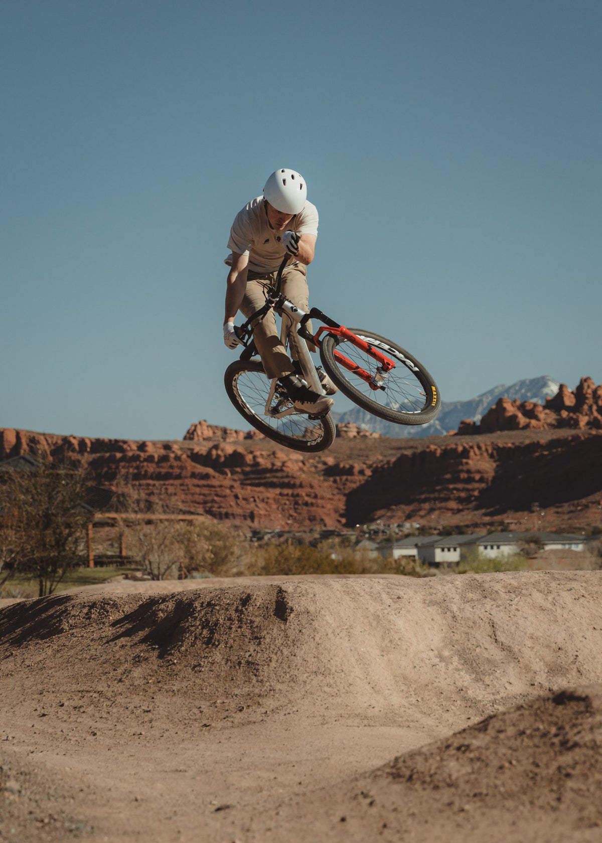 Rider airborne on an 801 dirt jump bike above desert jumps with red rock behind