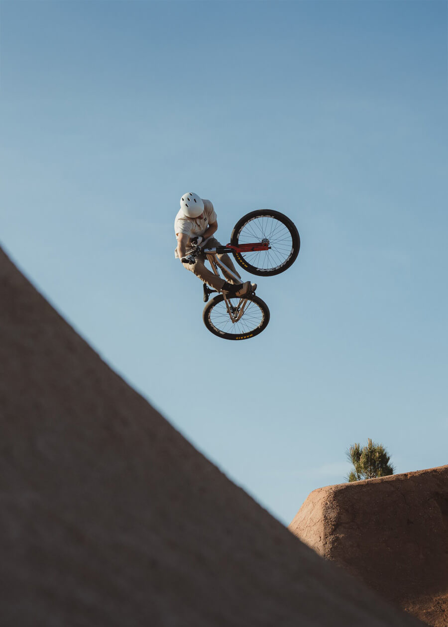 Rider and 801 dirt jump bike in the air above a dirt lip against a blue sky
