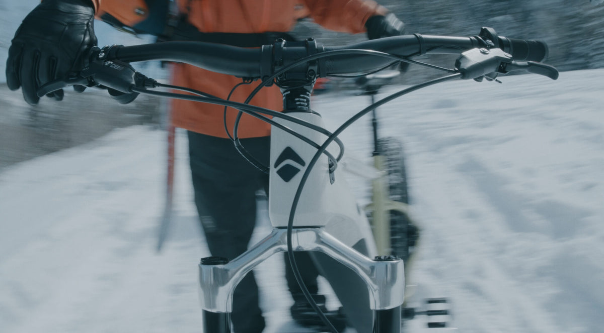 Rider in gloves walking a white Explorer Peak fat bike through snow, handlebar and fork visible