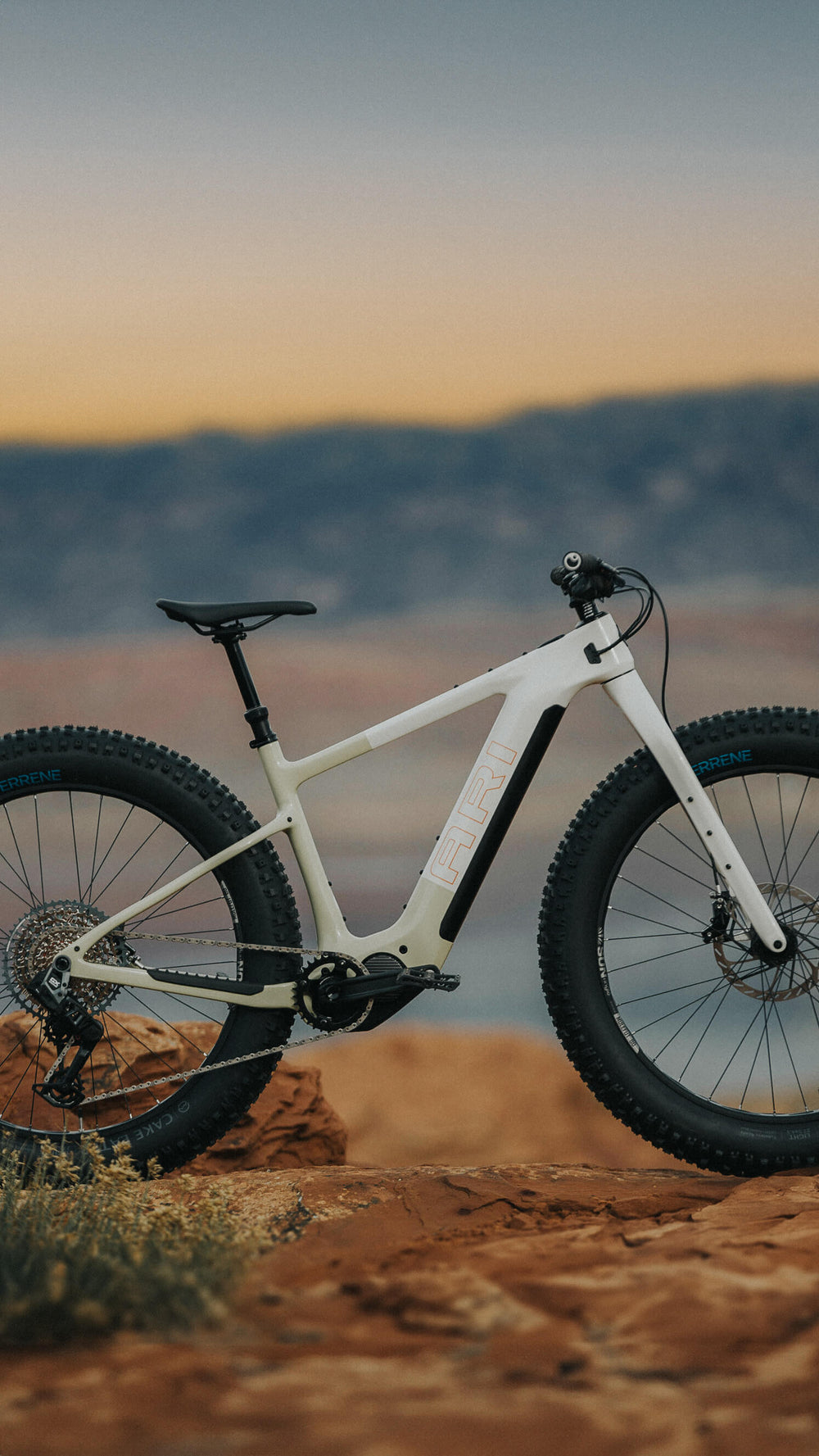 Vertical view of a white Explorer Peak fat electric bike on red rock at sunset