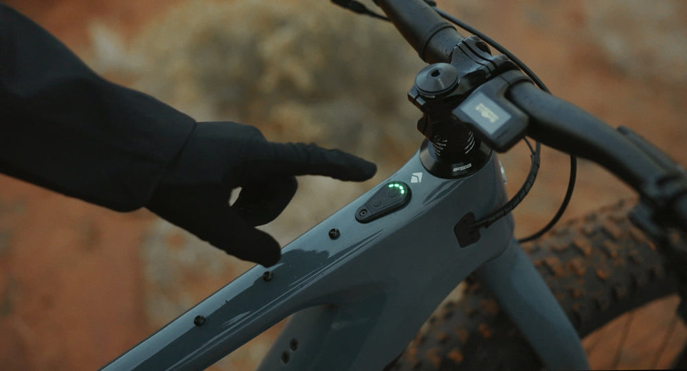 Gloved hand reaching for the glowing power button on the Explorer Peak top tube