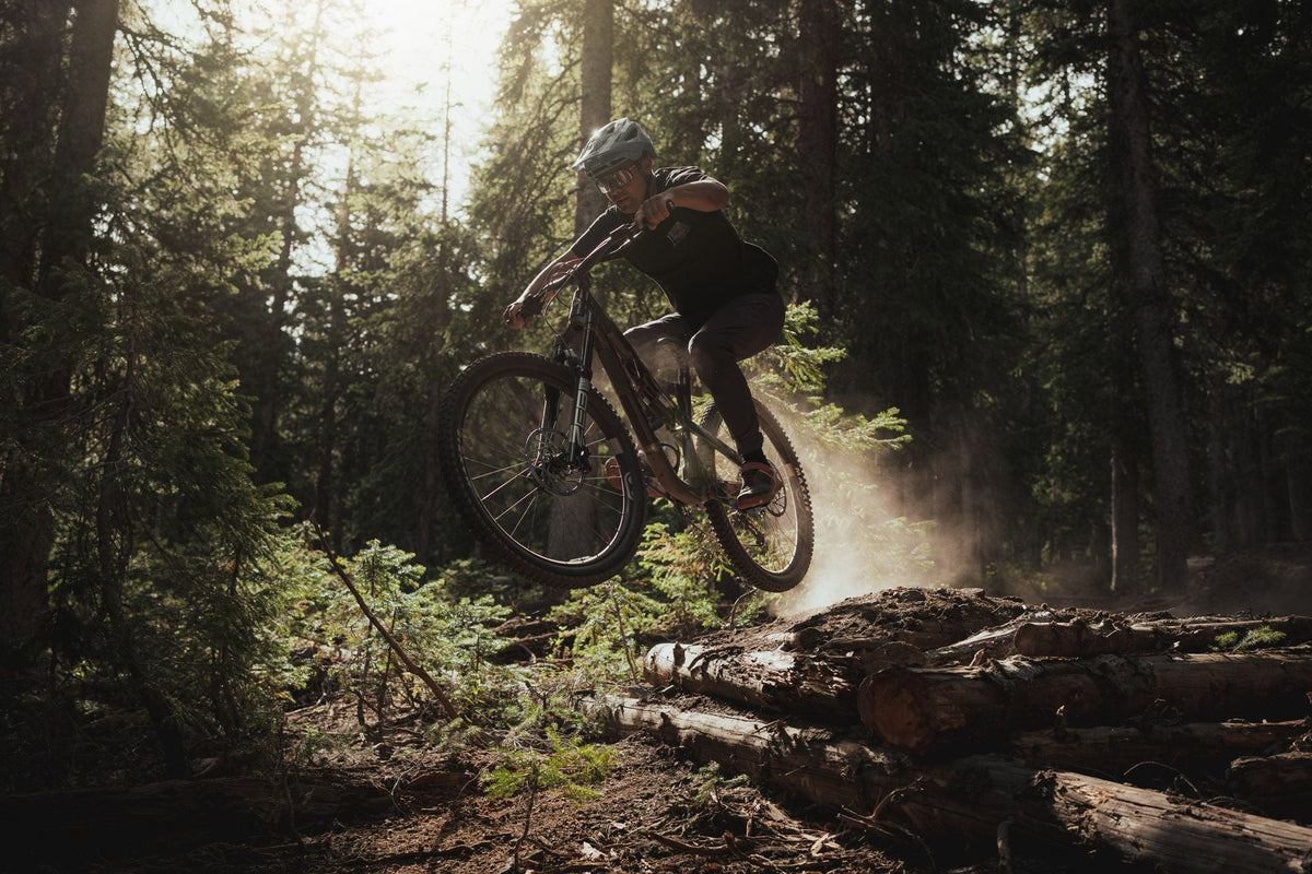 Rider jumping the La Sal Peak off a log pile in a sunlit forest