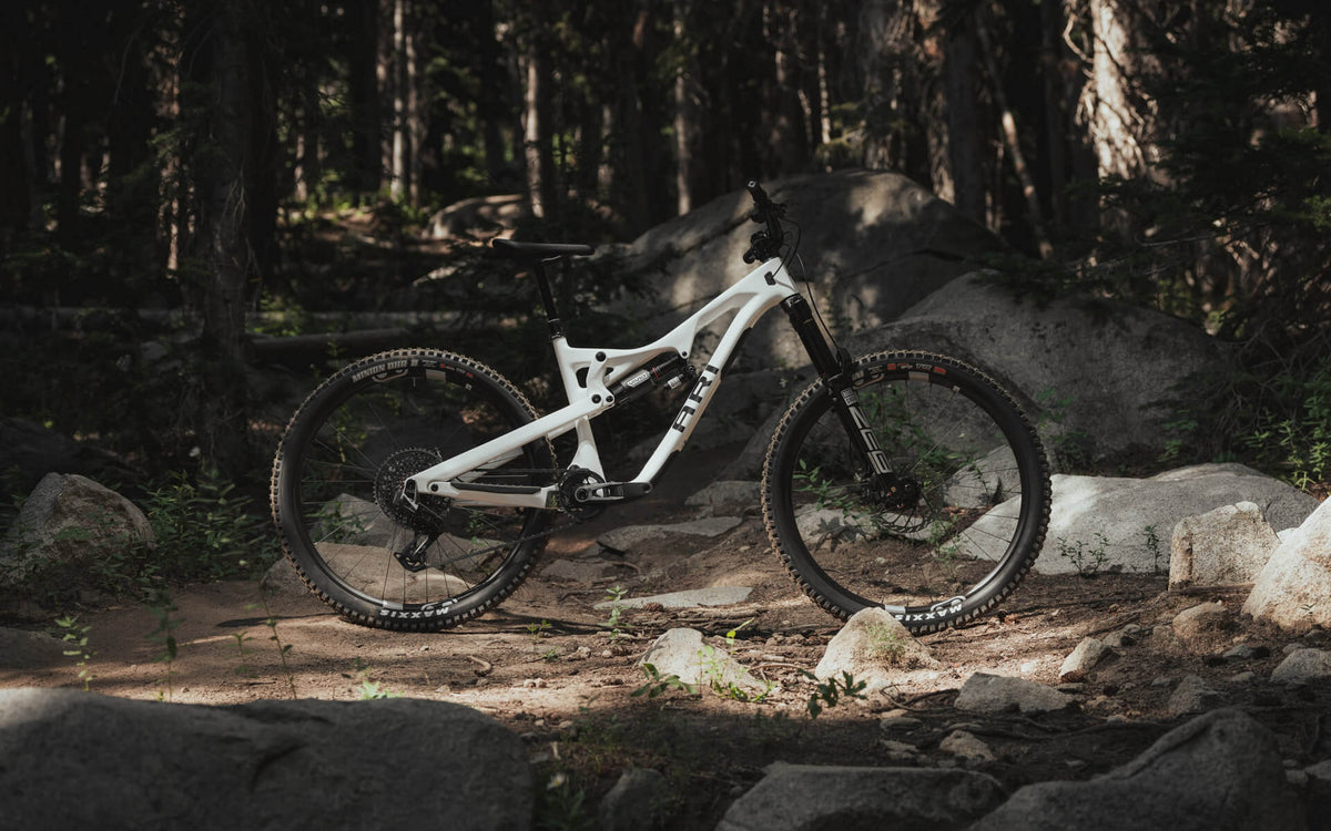 Ari La Sal full-suspension mountain bike in white standing among boulders in dim forest light