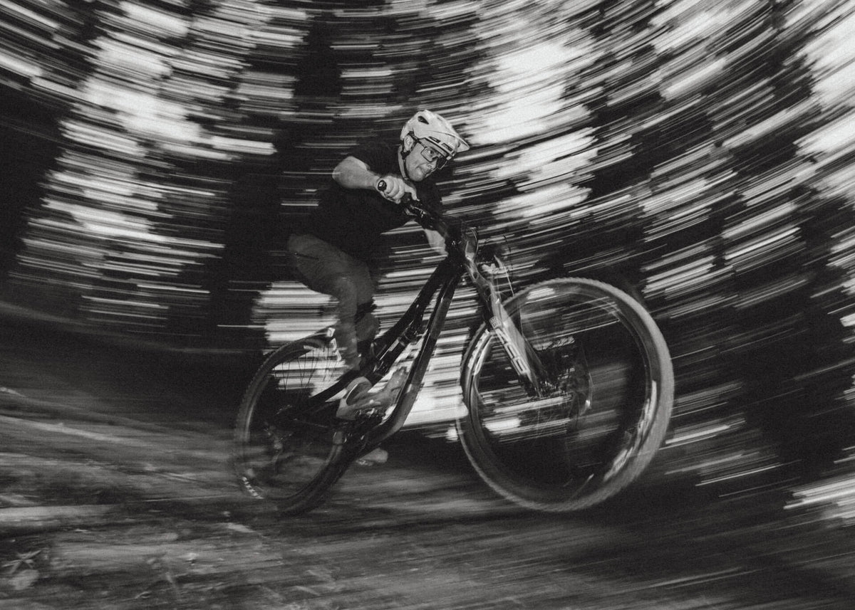 Black-and-white panning shot of a rider carving a corner on a full-suspension bike