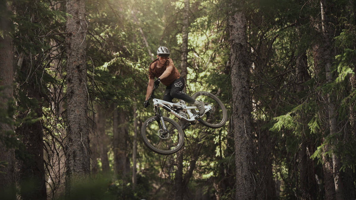Rider flying between pine trees on a white La Sal full-suspension bike