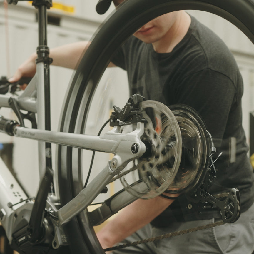 Mechanic in a gray tee working on the rear wheel and brake of a silver e-bike