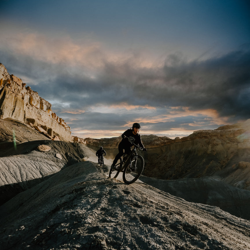 Rider climbing a rocky desert ridge at dusk with a second rider behind