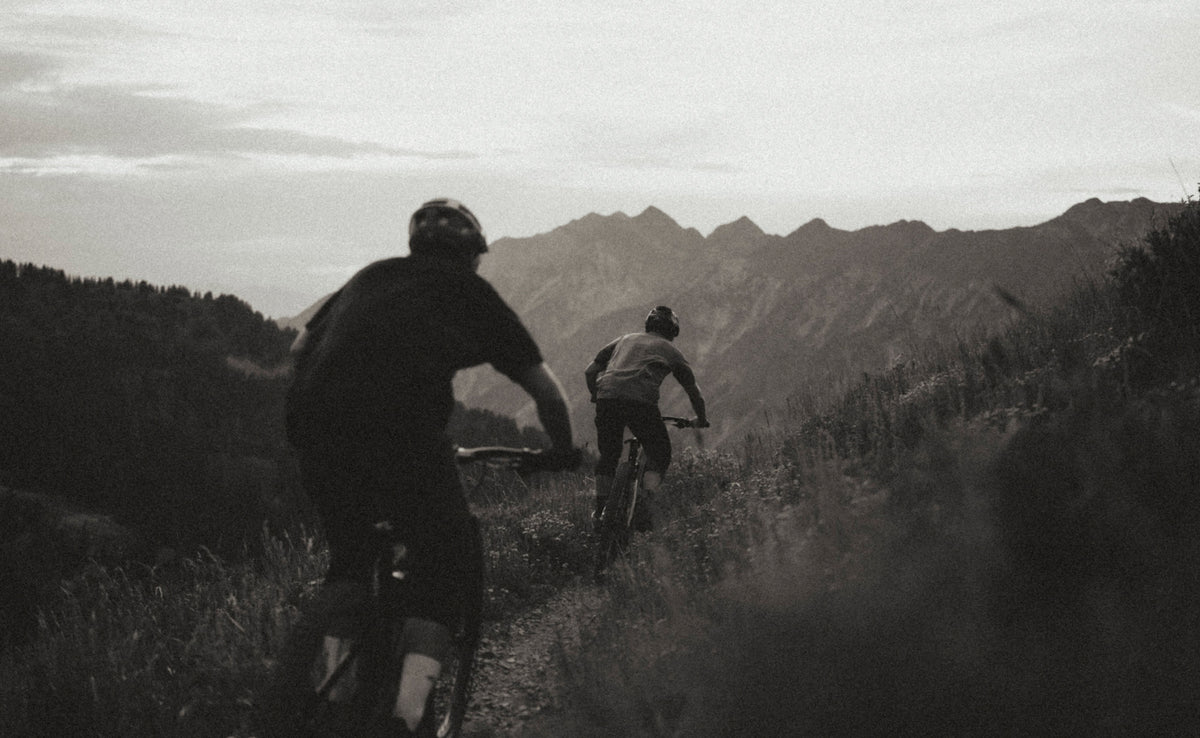 Black-and-white view from behind of two riders on mountain bikes on a ridge trail