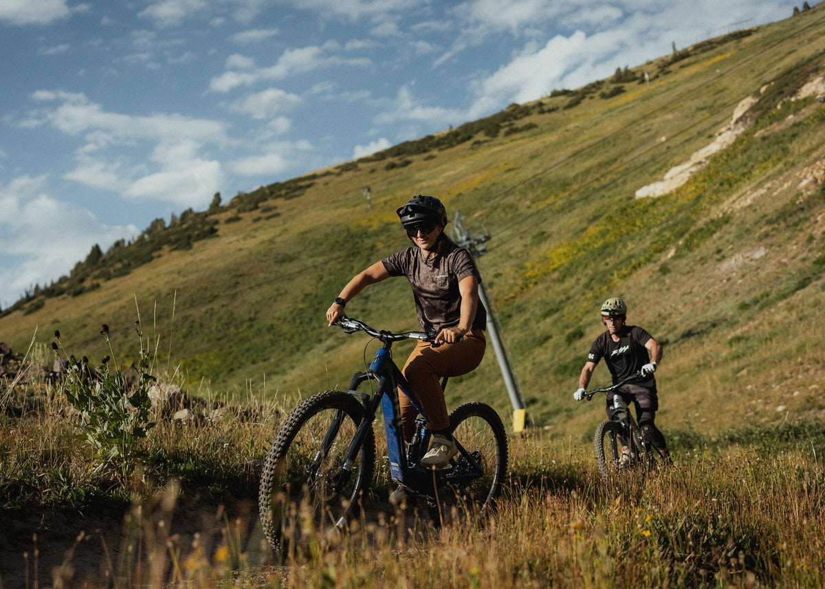 Two riders on e-mountain bikes descending a grassy mountain slope