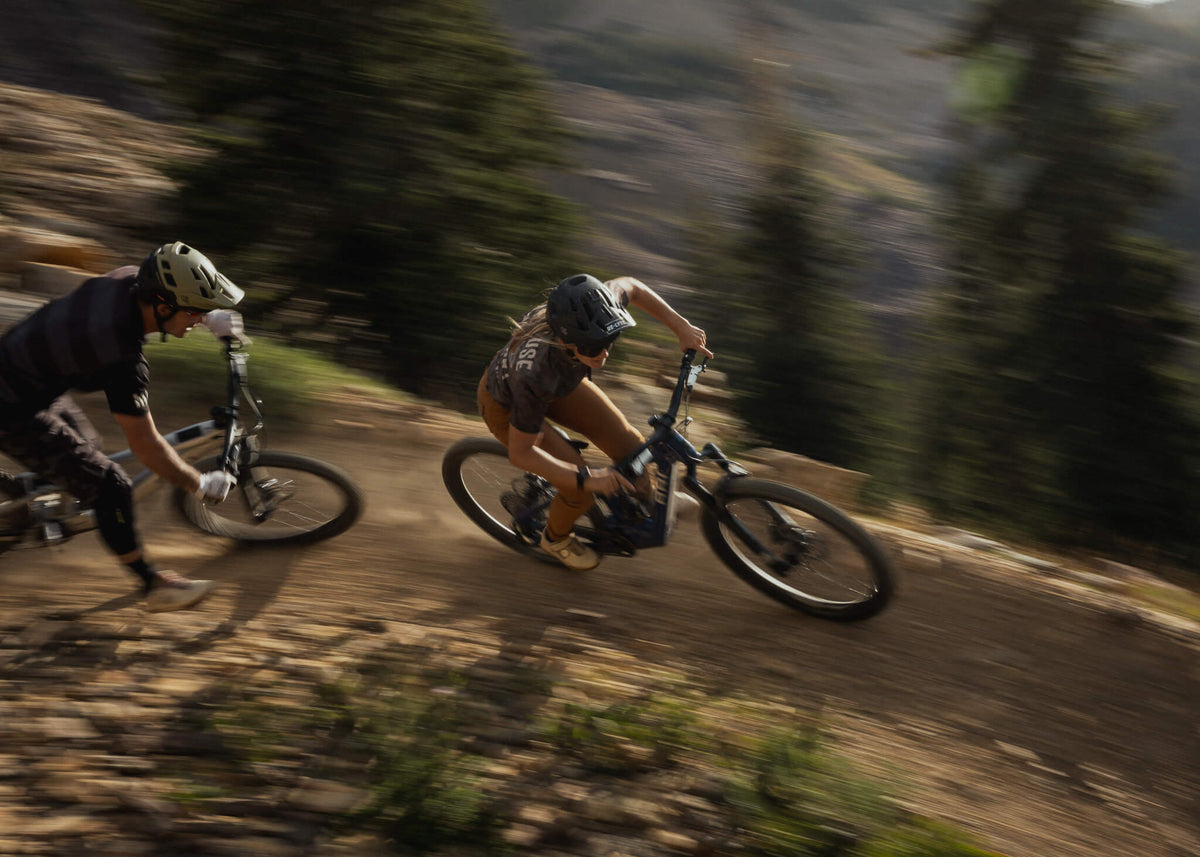 Two riders on e-mountain bikes descending a dirt trail in motion blur