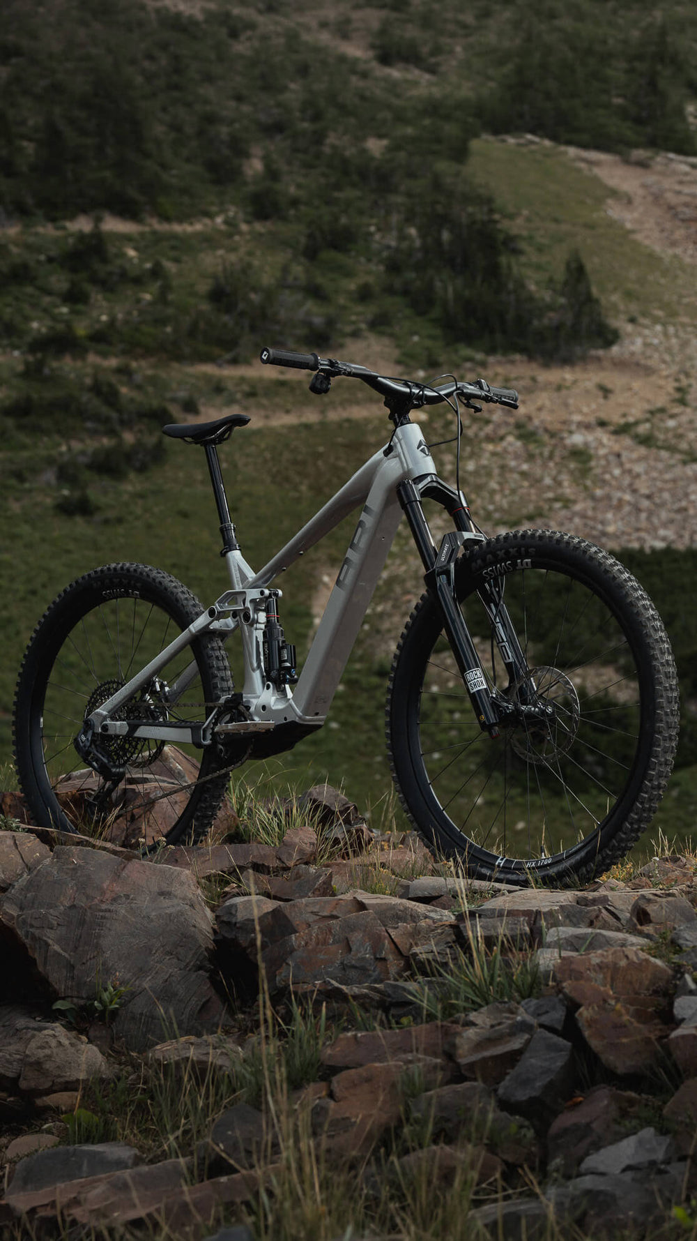 Gray Wire Peak e-bike standing on a rocky slope with green hills behind