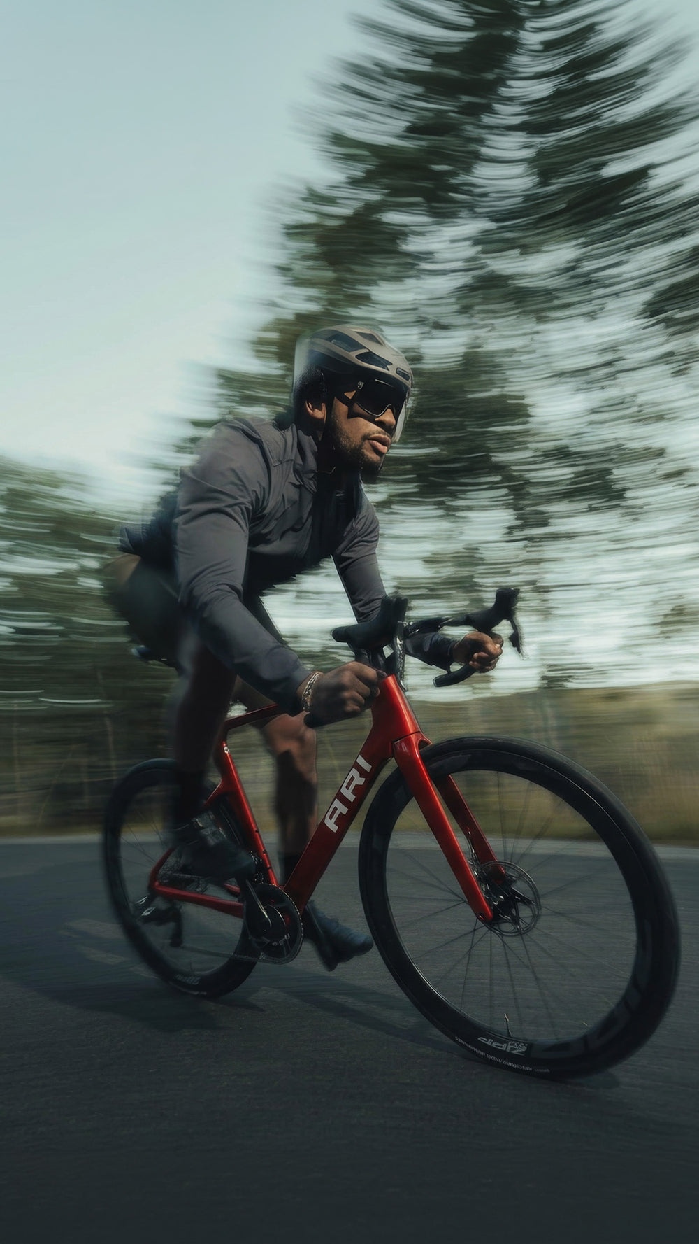 Rider on a red Ari Veyo road bike cornering on a paved road, vertical crop