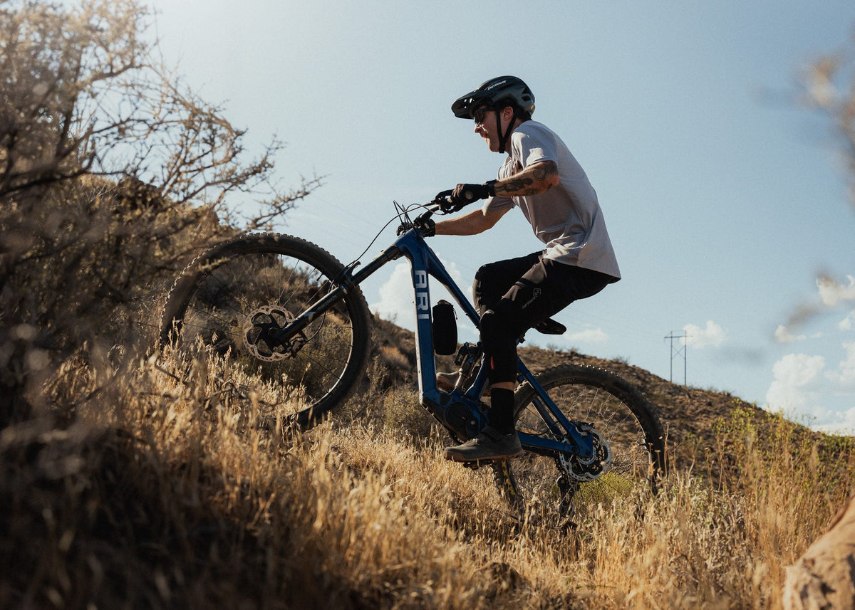 Rider climbing a dry hillside on a blue Ari Wire Peak